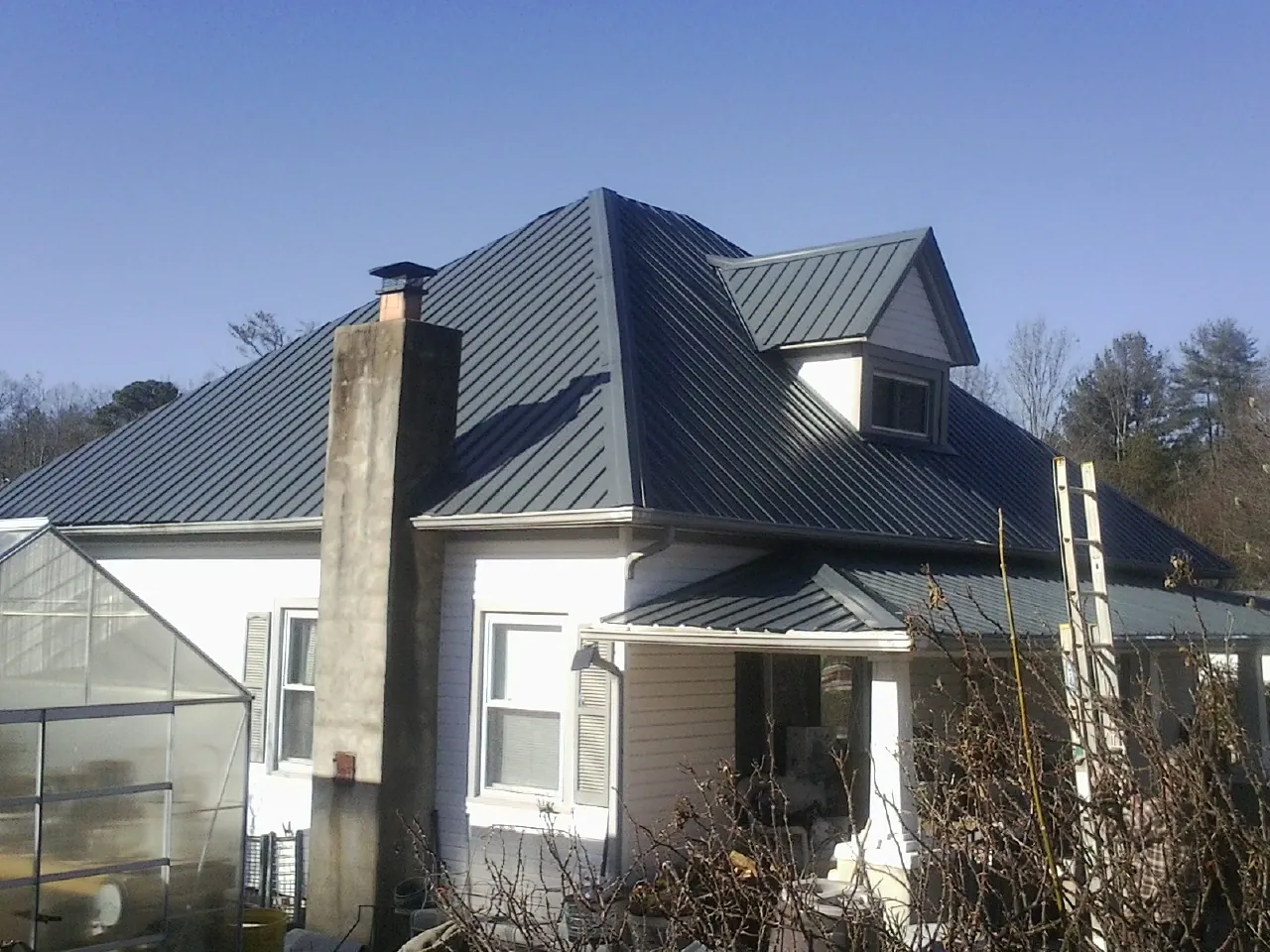 Dark blue standing seam metal roof on a white farmhouse with dormer — Slate & Tile Roof Repair by Roofing Brothers in Bailey