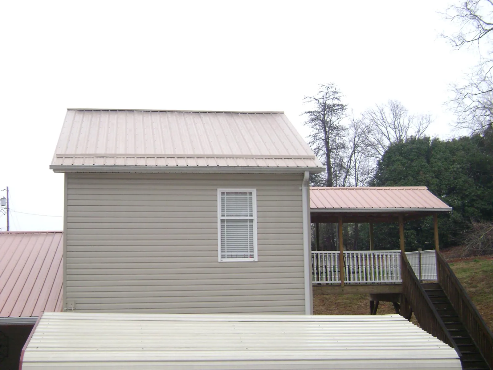 Tan metal roofs on a two story addition and attached porch, from a Roof Replacement job in Bailey